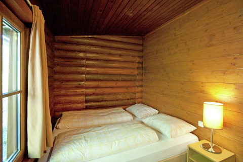 Bright bedroom with double bed, wooden walls, and bedside lamp in Chalet Catharina in Austria.
