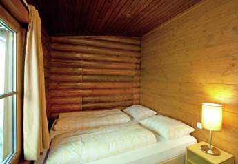 Bright bedroom with double bed, wooden walls, and bedside lamp in Chalet Catharina in Austria.
