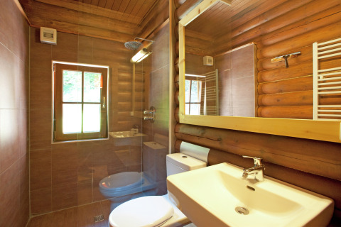 Modern bathroom with wood log walls, large mirror and window inside Chalet «Catharina im Brixental» in Austria.