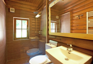 Modern bathroom with wood log walls, large mirror and window inside Chalet «Catharina im Brixental» in Austria.