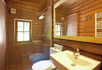 Modern bathroom with wood log walls, large mirror and window inside Chalet «Catharina im Brixental» in Austria.