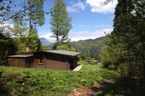 Chalet Catharina im Brixental in Austria, surrounded by green trees, hills and a small stream in foreground.