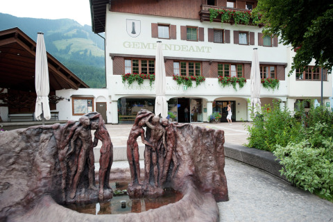 Sculpture in front of Chalet «Catharina im Brixental» in Austria, with flowers, mountains, and historic building.