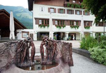 Sculpture in front of Chalet «Catharina im Brixental» in Austria, with flowers, mountains, and historic building.