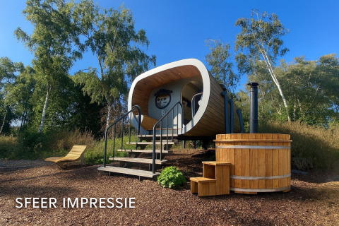Buitenaanzicht van een moderne tiny house genaamd Anthropod met houten hottub en ligstoel in de natuur.