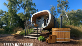 Vista exterior de una tiny house moderna llamada Anthropod, con bañera de madera y tumbona en plena naturaleza.