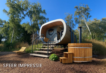 Vista esterna di una tiny house moderna chiamata Anthropod con tinozza in legno e sdraio immersi nella natura.