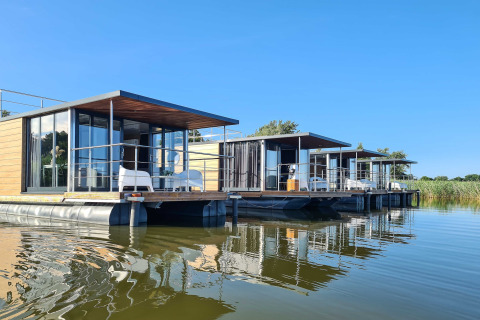 Modern houseboats on calm water in Denmark, designed for two people, with blue sky and relaxing views.