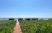 Houten pad door hoog gras naar woonboten op het water onder een blauwe lucht in Denemarken.