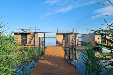 Drijvend huis voor 2 personen op het water in Denemarken, houten pad, riet, en heldere blauwe lucht.