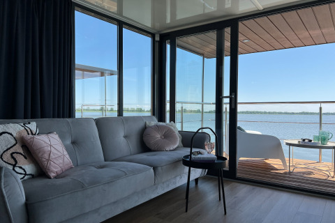 Modern houseboat living room with sofa and glass doors opening to a terrace overlooking the water in Denmark.