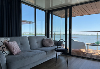 Moderne woonboot met sofa en glazen deuren naar terras met zicht op het water in Denemarken.