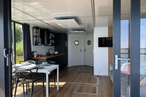 Modern interieur van een woonboot in Denemarken met eettafel, keuken en zicht op het water.
