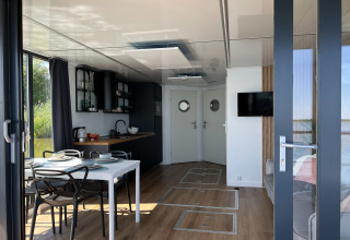 Modern woonbootinterieur in Denemarken met eettafel, keuken, grote ramen en uitzicht op het water.