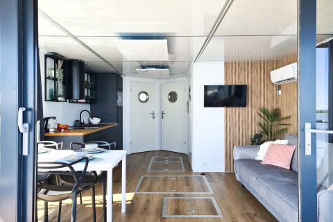 Modern houseboat in Denmark with open kitchen, dining table, sofa, TV, and cozy decor for two guests.