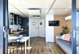 Modern houseboat in Denmark with open kitchen, dining table, sofa, TV, and cozy decor for two guests.