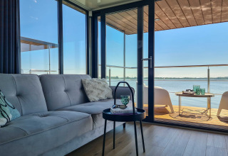 Houseboat living room with sofa and table, opening to a deck overlooking the water in Denmark.