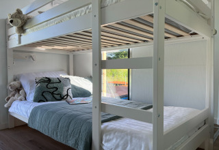 Modern wooden bunk bed in a bright room aboard a Danish houseboat, view of greenery through window.