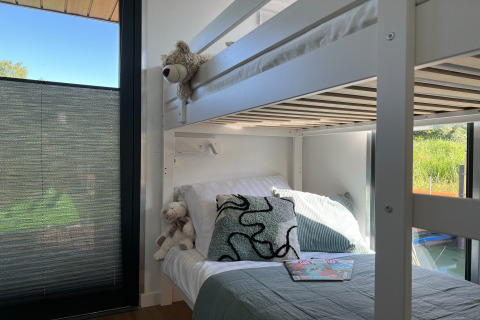 Modern stapelbed met kussens en knuffels aan groot raam op woonboot in Denemarken, zonlicht stroomt binnen.