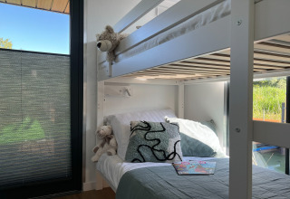 Modern stapelbed met kussens en knuffels aan groot raam op woonboot in Denemarken, zonlicht stroomt binnen.