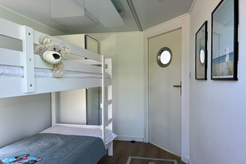 Bright houseboat bedroom with white bunk beds, a plush teddy bear, and a modern door with porthole.