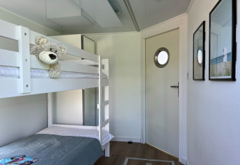 Bright houseboat bedroom with white bunk beds, a plush teddy bear, and a modern door with porthole.