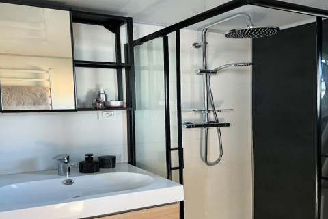 Modern bathroom on a houseboat in Denmark featuring a shower, sink, mirror, and shelves.