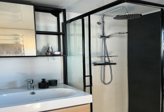 Moderne badkamer op een woonboot in Denemarken met een douche, wastafel, spiegel en rekjes.