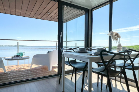 Moderne woonboot in Denemarken met eetruimte en terras met zicht op het water onder een heldere hemel.