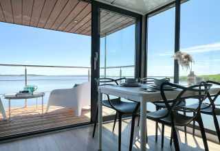 Moderne woonboot in Denemarken met eetruimte en terras met zicht op het water onder een heldere hemel.