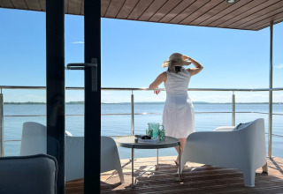 Vrouw in witte jurk met hoed op terras van woonboot voor twee personen genietend van uitzicht in Denemarken.