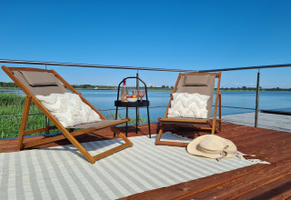 Relaxing houseboat deck with two lounge chairs, pillows, table, and scenic lake view in Denmark.