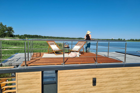 Vrouw geniet van het uitzicht op het dakterras van een woonboot voor 2 aan een meer in Denemarken.