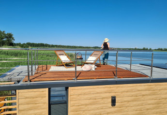 Vrouw geniet van het uitzicht op het dakterras van een woonboot voor 2 aan een meer in Denemarken.
