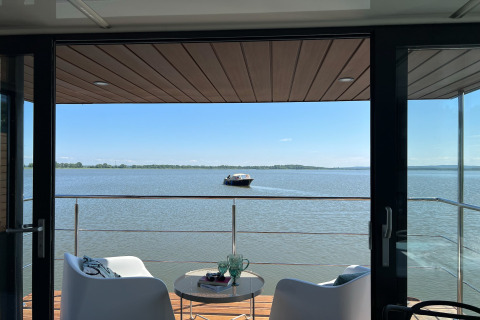 Zicht vanaf woonboot 'House on the water for 2 people' in Denemarken, terras met stoelen en boot op het meer.