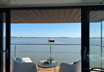 Zicht vanaf woonboot 'House on the water for 2 people' in Denemarken, terras met stoelen en boot op het meer.