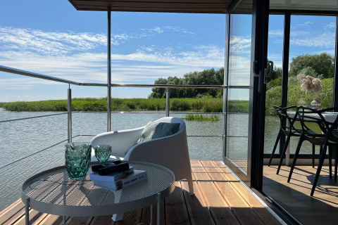 Uitzicht vanaf een woonbootterras in Denemarken met stoel en tafel aan het water voor twee personen.