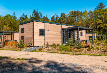 Moderna Groeneborg lodge con vasca idromassaggio, circondata da alberi e natura sotto il cielo blu.
