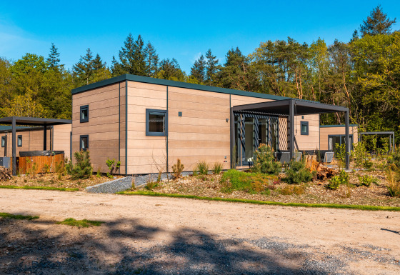 Moderne Groeneborg lodge met hottub, omringd door bomen en groen, onder een heldere blauwe lucht.