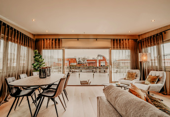 Lichte woonkamer op woonboot ‘Woude’ in Marina Uitgeest, Nederland, met zicht op water en huisjes.