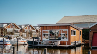 Houseboat Woude docked on the water, surrounded by modern houses and boats under a clear sky.