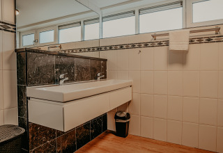 Moderne badkamer met dubbele wasbak, grote spiegel en zwarte tegeldetails op een woonboot in Nederland.
