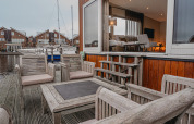 Udendørs træterrasse med komfortable stole på husbåd 'Woude' ved Marina Uitgeest, Nederlandene.