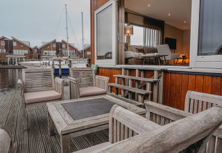 Udendørs træterrasse med komfortable stole på husbåd 'Woude' ved Marina Uitgeest, Nederlandene.