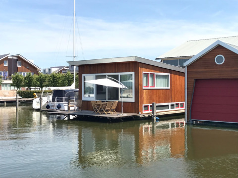 Woonboot «Woude» aan Marina Uitgeest in Nederland, met terras, parasol en kalme waterrijke omgeving.