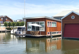Hausboot «Woude» an der Marina Uitgeest in den Niederlanden mit Terrasse, Sonnenschirm und ruhigem Wasser.