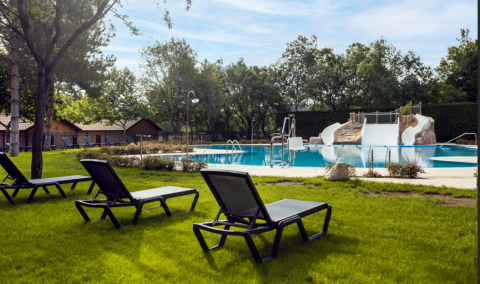 Liegestühle auf Rasen neben Pool mit Wasserrutschen im Wecamp Pirineos Ferienpark, Aragón, Spanien.