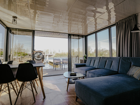 Modern living room in Houseboat 'Campi' at Marina Uitgeest, Netherlands, with large windows and water view.