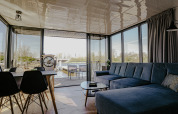 Modern living room in Houseboat 'Campi' at Marina Uitgeest, Netherlands, with large windows and water view.
