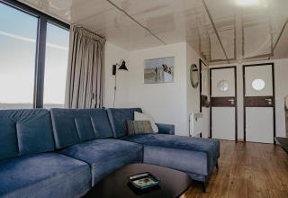 Salon sur la péniche « Campi » à Marina Uitgeest aux Pays-Bas avec canapé bleu et vue sur l'eau.
